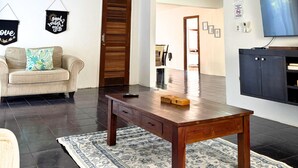 A spacious living room with a wooden coffee table, a sofa, a TV mounted on the wall, and a ceiling fan. - Cozy Beach Home with Pool, Game Room & Gym – Walk to the Beach (Dorado)