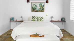 A bedroom with a bed, a nightstand, a wall-mounted air conditioner, a framed painting, and a window with blinds. - Cozy Beach Home with Pool, Game Room & Gym – Walk to the Beach (Dorado)