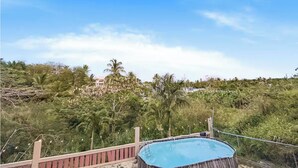 A pool area with a view of a tropical landscape, including palm trees and a hill in the background. - Cozy Beach Home with Pool, Game Room & Gym – Walk to the Beach (Dorado)