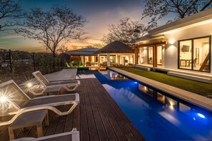 Un espace piscine extérieur moderne, doté de chaises longues et d’une terrasse en bois.