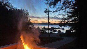 Een houtkachel op een houten terras, met uitzicht op een meer en bergen op de achtergrond.