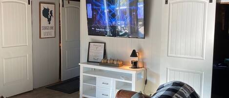 Een gezellige woonkamer met een grote televisie, houten balken, een witte console tafel en een comfortabele bank.