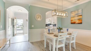 A dining area with a white table and chairs, a hanging light fixture, a clock, and a painting on the wall. - 3 Mi to Barefoot Landing: Condo w/ 2 Pools! (North Myrtle Beach)
