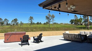 Een terras buiten met een overdekte zithoek, een jacuzzi en uitzicht op een golfbaan.