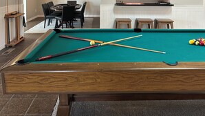 Een biljart met keuen en ballen, een eethoek met stoelen en een tafel, en een keuken met kastjes en een aanrecht.