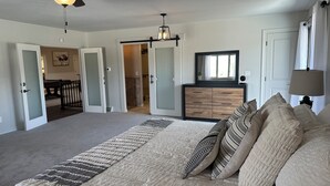 Een slaapkamer met een bed, een dressoir, een plafondventilator en een gang naar een badkamer.