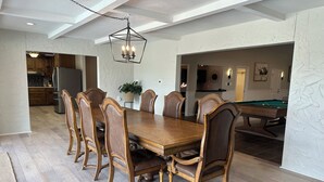 Een eetruimte met een houten tafel en stoelen, een kroonluchter en een biljarttafel op de achtergrond.