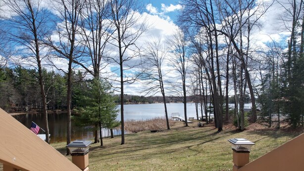 A lakeside view with a wooden deck, a flag, and a bench. - Lake Nokomis  Cozy 2-Bed Getaway for Couples, Families & Outdoor Enthusiasts (Tomahawk)