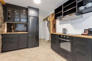 A modern kitchen with dark cabinetry, a stainless steel refrigerator, a built-in oven, and a wooden countertop.
