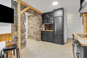A modern kitchen with a stone wall, wooden beams, a black refrigerator, and a wooden countertop.