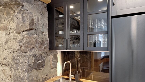 A kitchen with a stone wall, a stainless steel sink, and dark cabinets with glass doors. - Ranargata - Central Four Bedrooms Apartment A (Reykjavík)