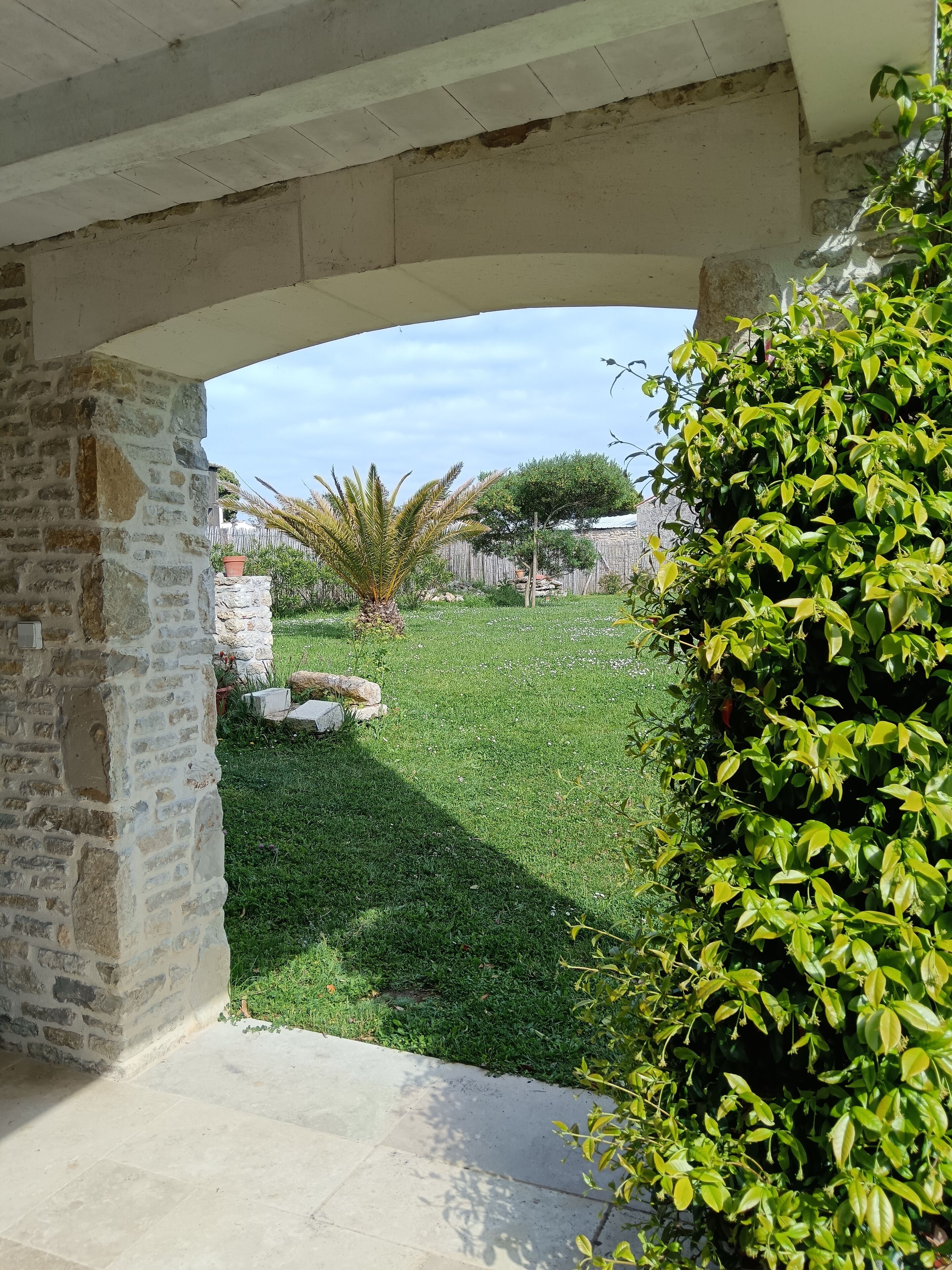 Un espace extérieur aménagé en terrasse, avec un mur en pierre, une pelouse et une vue sur une propriété clôturée.
