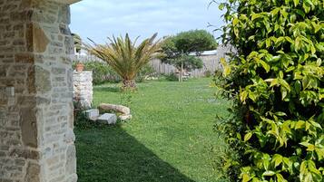 Un espace extérieur aménagé en terrasse, avec un mur en pierre, une pelouse et une vue sur une propriété clôturée.