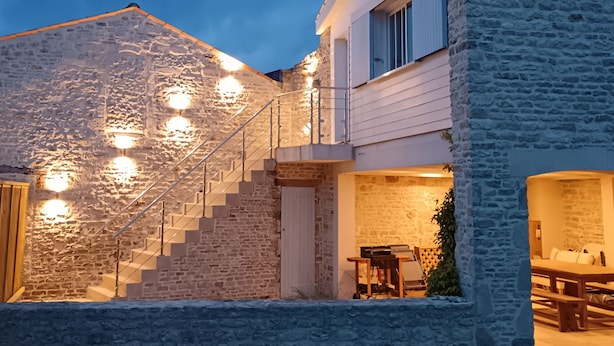 Ein Steinhaus mit einer Treppe zum zweiten Stock, einem Essbereich mit Tisch und Stühlen und einem kleinen Garten.
