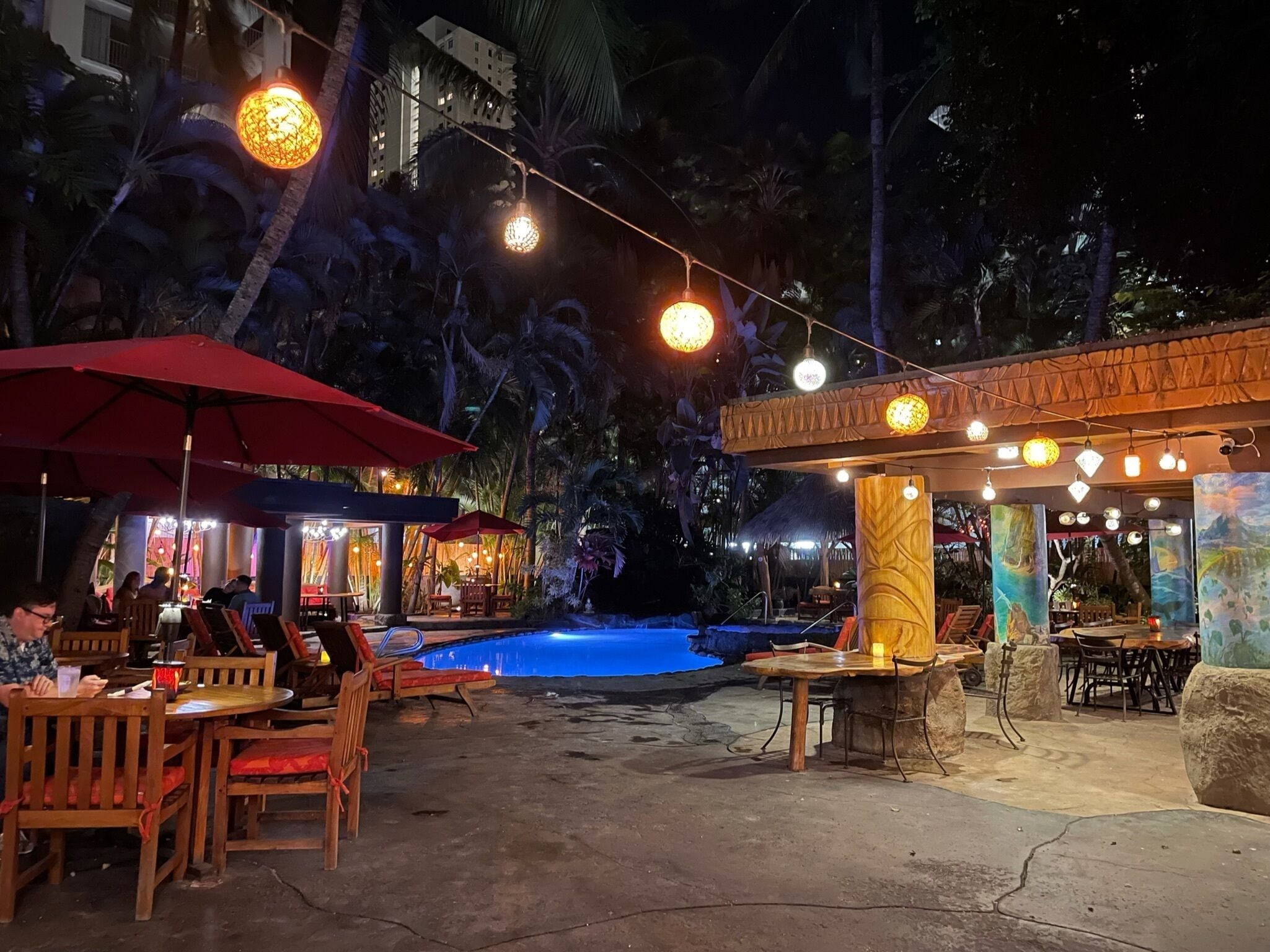 Un espace extérieur aménagé pour les repas, avec des tables et des chaises, une piscine et des plantes tropicales.