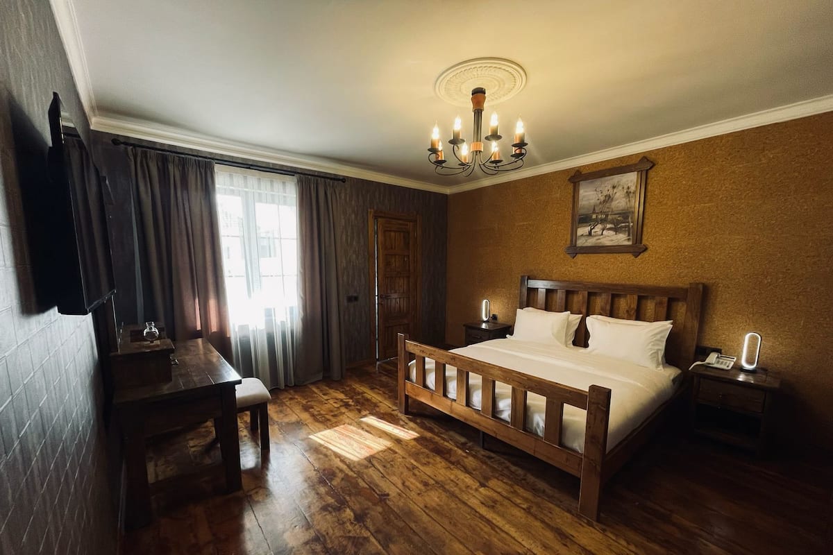 Quarto com cama de madeira, mesa de cabeceira, luminária e janela com cortinas.