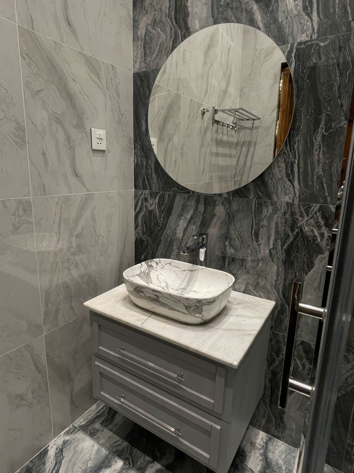 A bathroom with a marble sink, a round mirror, and a towel rack.