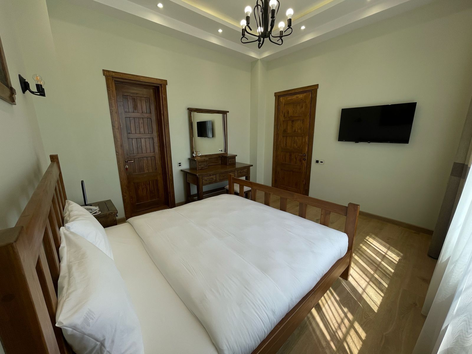 A bedroom with a wooden bed, a dresser, a mirror, and a television on the wall.