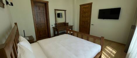 A bedroom with a wooden bed, a dresser, a mirror, and a television on the wall.