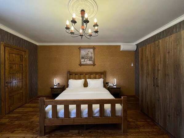 A wooden-framed bed with white linens, a wooden wardrobe, a wooden door, and a wall-mounted painting. - Magnolia Family Boutique and Spa (Ismailli)