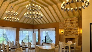 A dining area with multiple tables and chairs, a brick fireplace, and a vaulted ceiling with chandeliers. - Magnolia Family Boutique and Spa (Ismailli)
