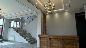 A spacious room with a herringbone-patterned floor, a wooden reception desk, a staircase, and a chandelier. - Magnolia Family Boutique and Spa (Ismailli)