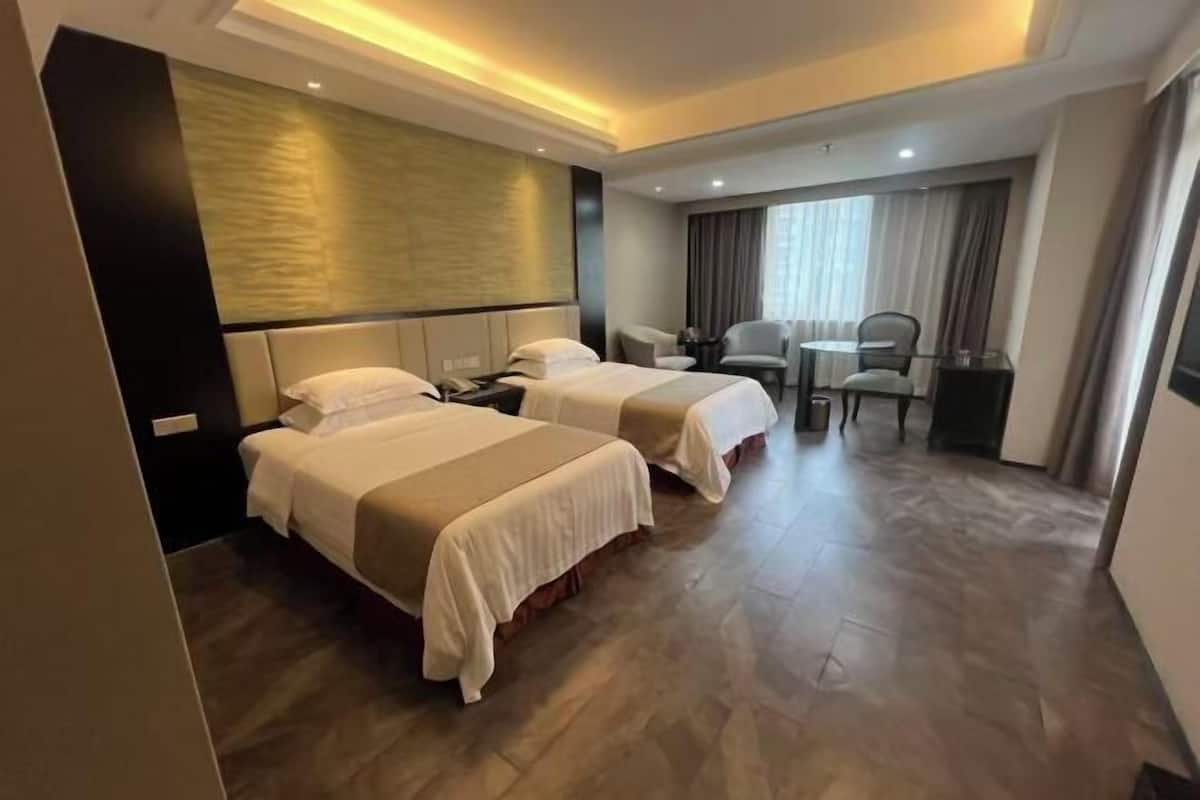 A hotel room with two beds, a desk, a chair, and a large window.