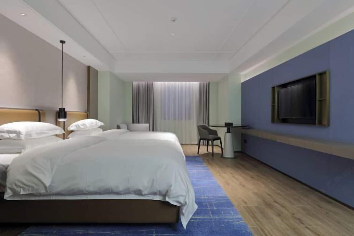 A hotel room with a large bed, a desk, a chair, a TV, and a window with curtains.