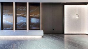 A modern interior with a reception desk, large windows with artwork, and a hanging light fixture.