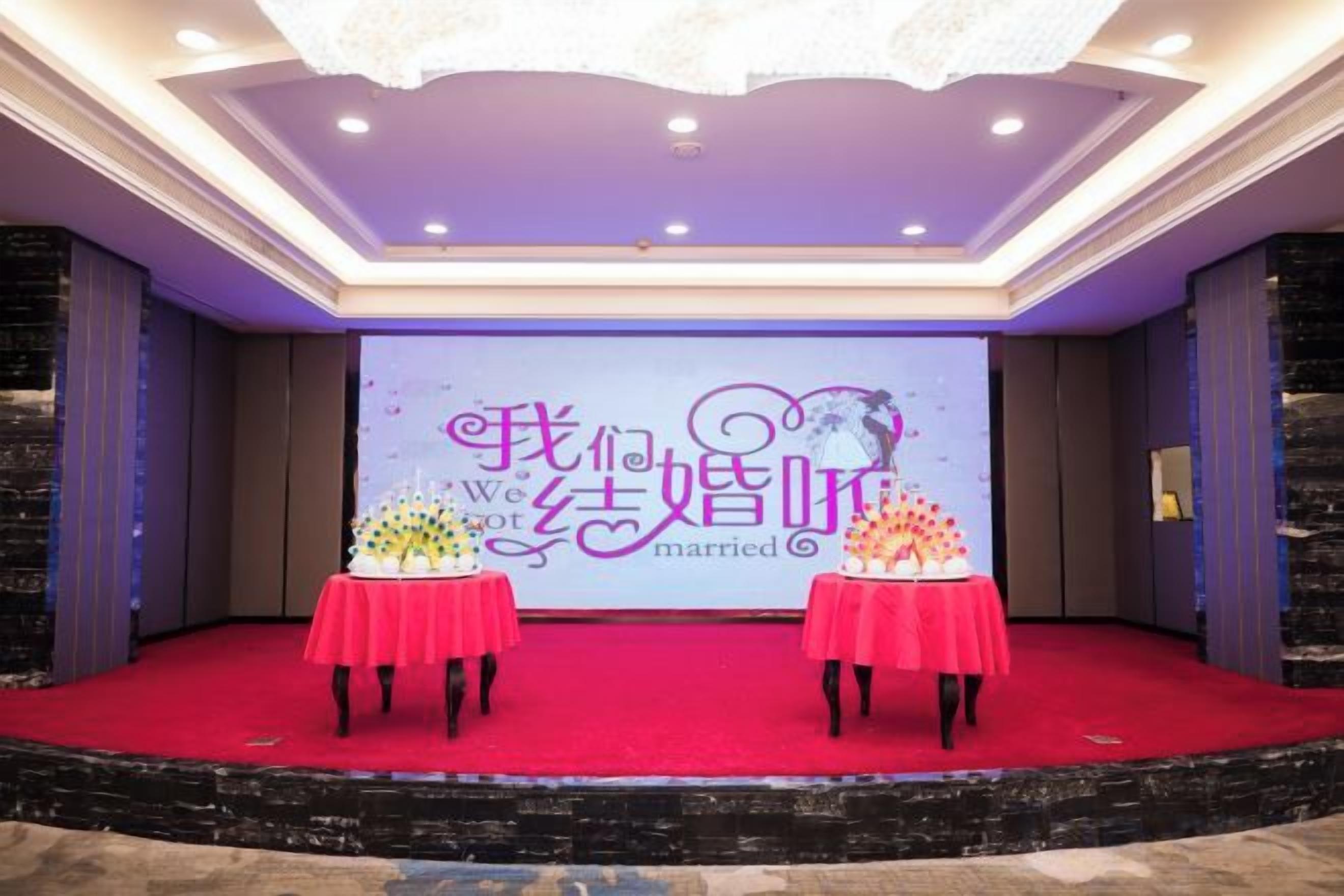 A stage with a backdrop for a wedding event, two tables with red tablecloths, and a red carpet.