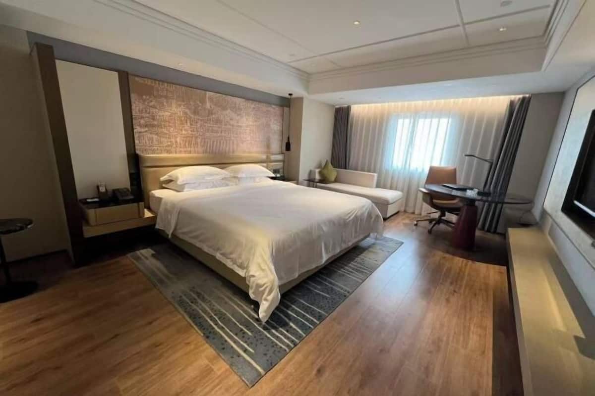 A hotel room with a large bed, a desk, a chair, a TV, and a window with curtains.