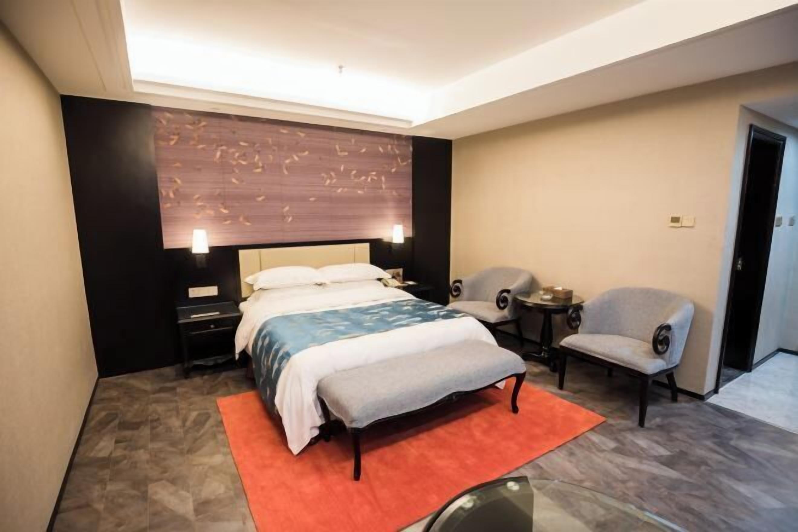 A modern hotel room with a large bed, a small side table, a chair, and a wall-mounted TV.