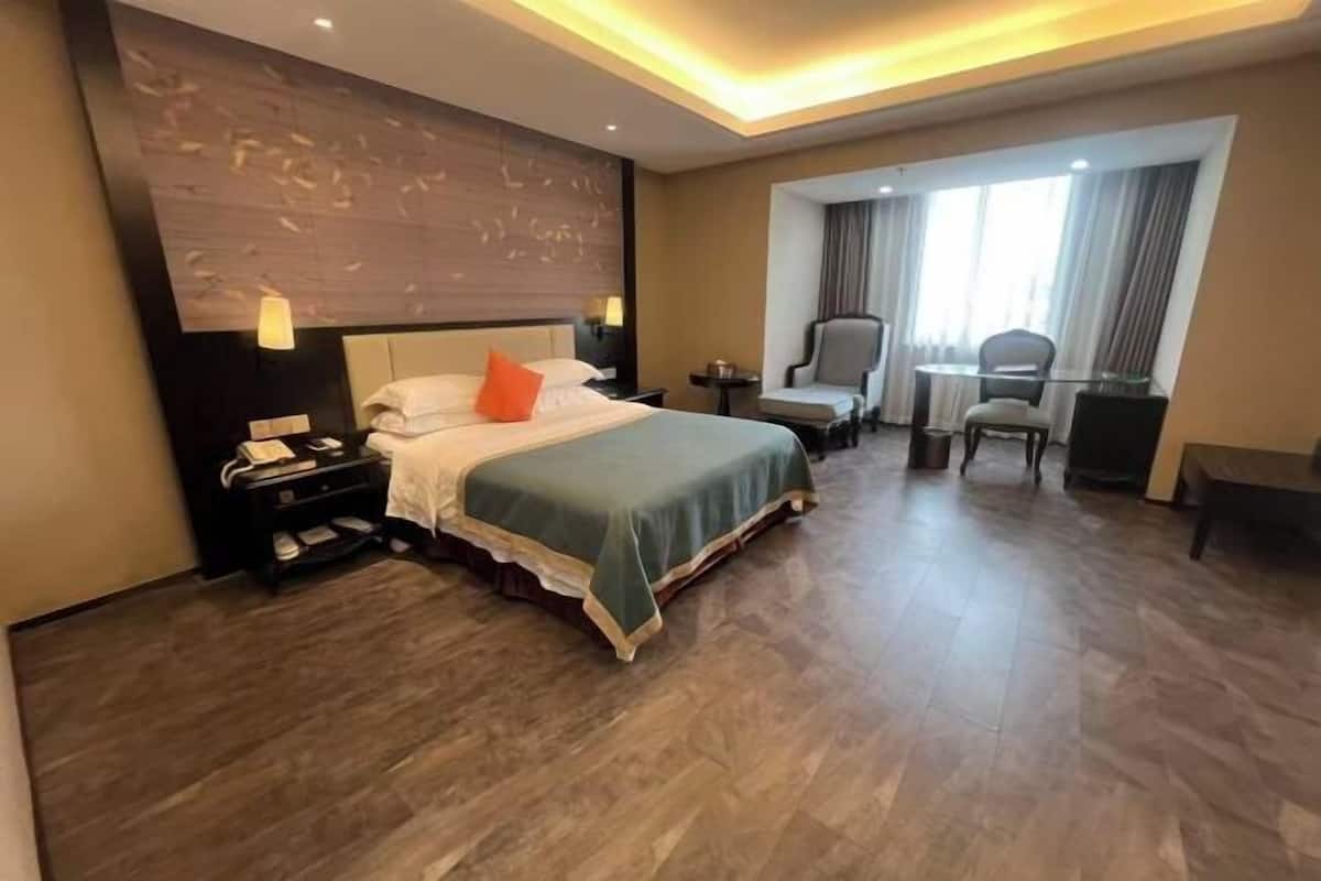 A hotel room with a large bed, a desk, a chair, and a window.