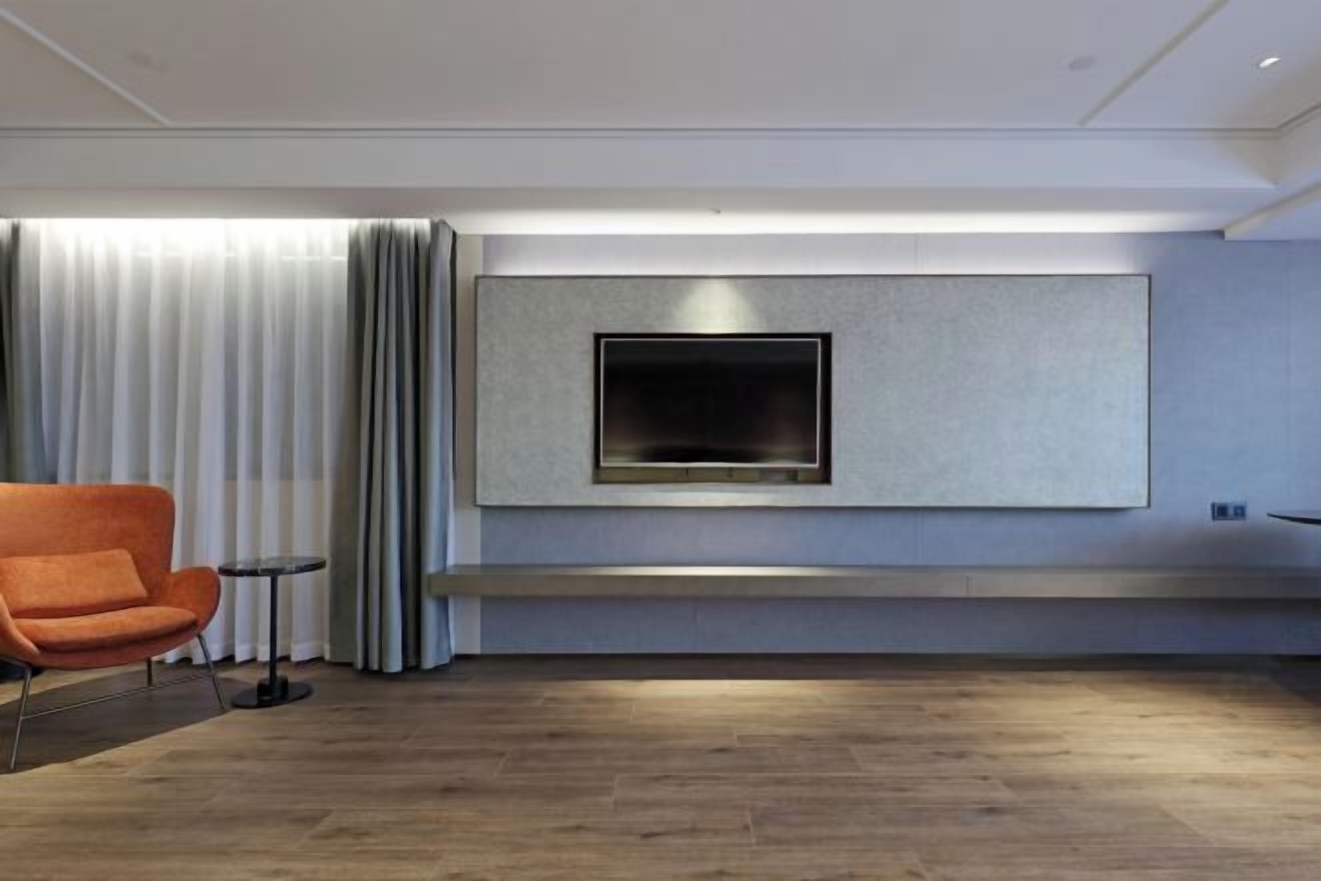 Un salon moderne avec un téléviseur fixé au mur, un canapé, une petite table et une fenêtre avec des rideaux.