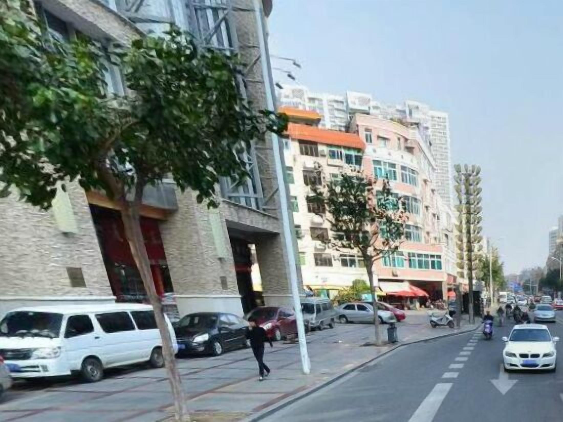 A street with parked cars and a pedestrian walking on the sidewalk.