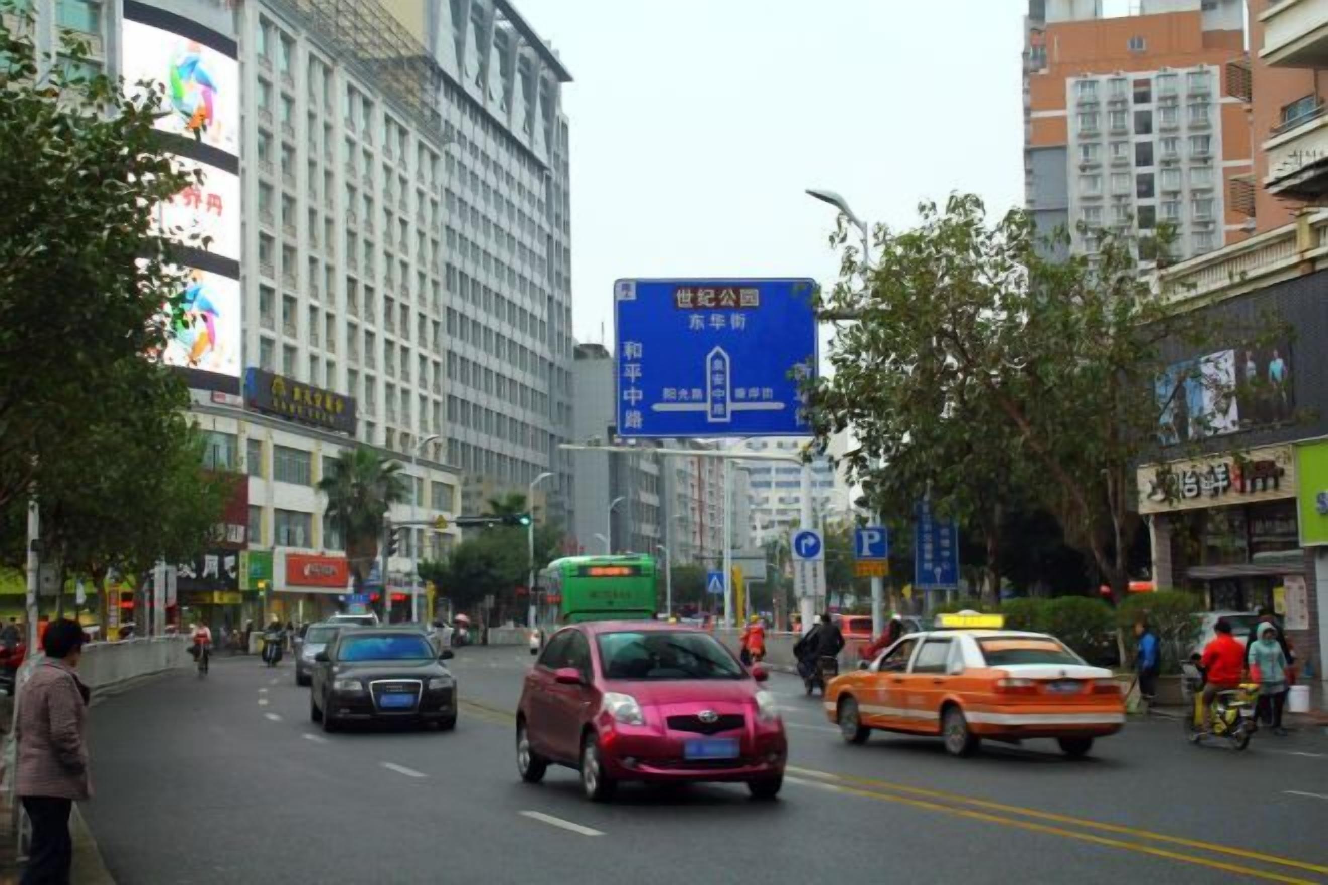 Eine belebte Stadtstraße mit Fahrzeugen, Fußgängern und Geschäftsgebäuden.