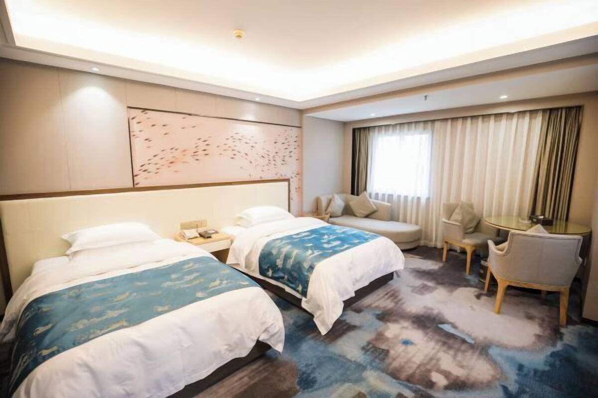 A hotel room with two beds, a sofa, a small table, and a chair.