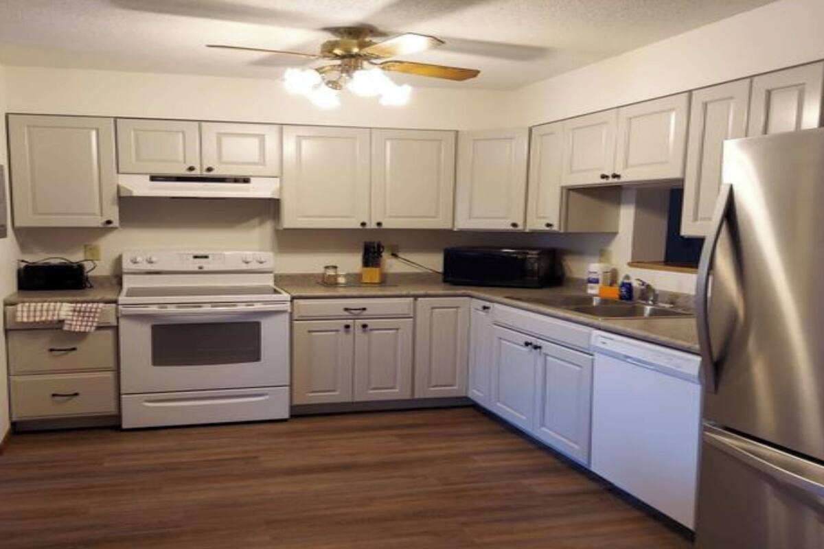 A kitchen with white cabinets, a stainless steel refrigerator, a microwave, an oven, and a ceiling fan.
