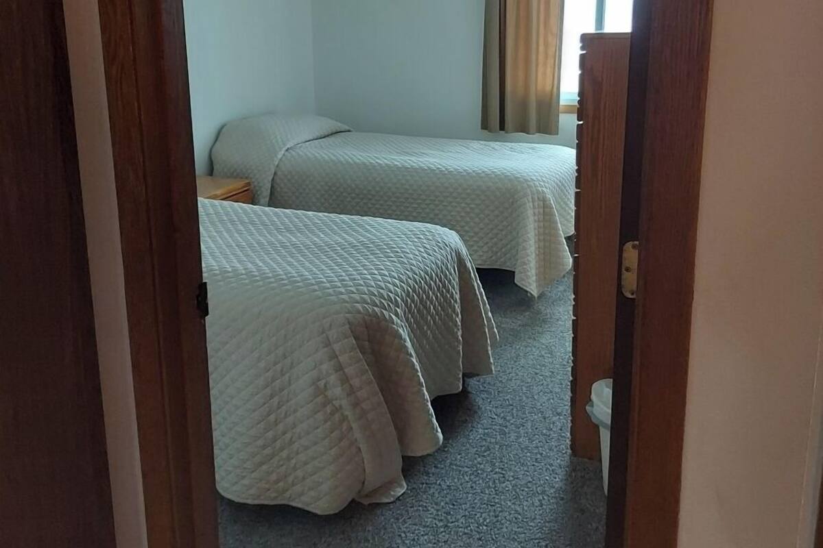 A room with two beds, a ceiling fan, and a window with curtains.