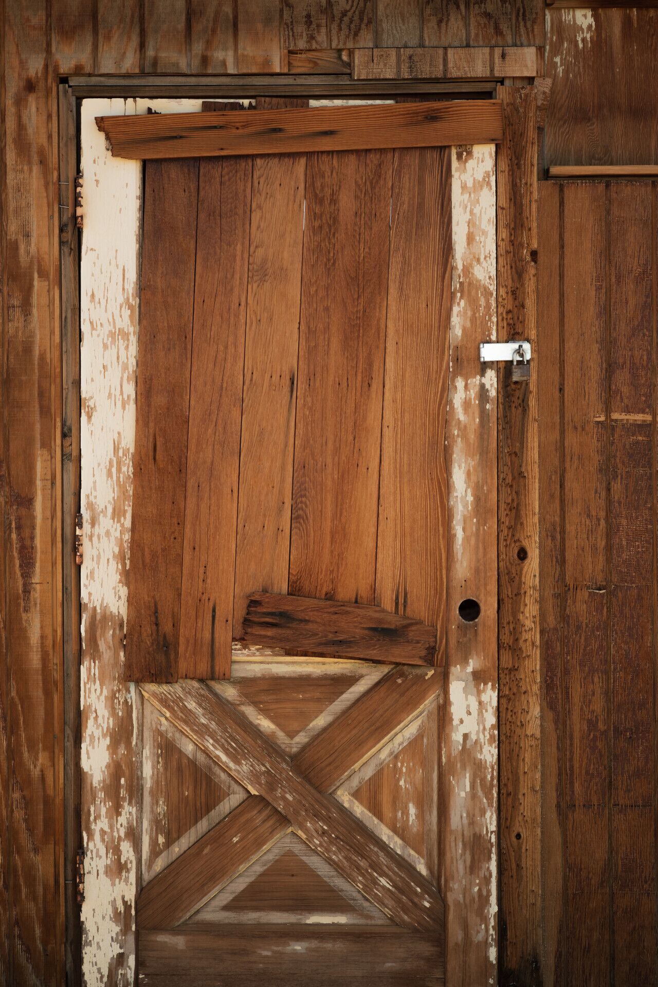 A rustic wooden door with a metal latch and a cross-patterned floor design.
