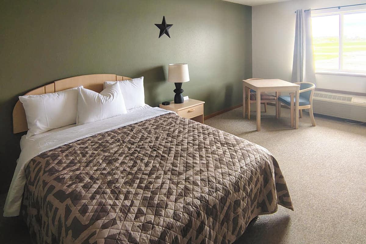 A hotel room with a bed, a nightstand, a desk, and a chair.
