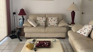 A living room with a beige sofa, a coffee table, a framed picture on the wall, and a door with a wreath. - Hibiscus Point - Villa for 4 pers. with large terrace, garden and heated pool (Lehigh Acres)