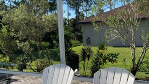 Two white Adirondack chairs on a paved patio with a grassy area and a building in the background. - Hibiscus Point - Villa for 4 pers. with large terrace, garden and heated pool (Lehigh Acres)