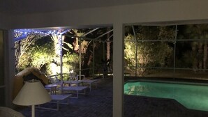 An outdoor patio area with a pool, lounge chairs, and a pergola with string lights. - Hibiscus Point - Villa for 4 pers. with large terrace, garden and heated pool (Lehigh Acres)