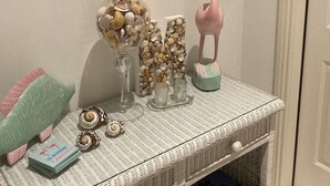 A room with a wicker console table displaying decorative items, a wreath on the wall, and a door. - Hibiscus Point - Villa for 4 pers. with large terrace, garden and heated pool (Lehigh Acres)
