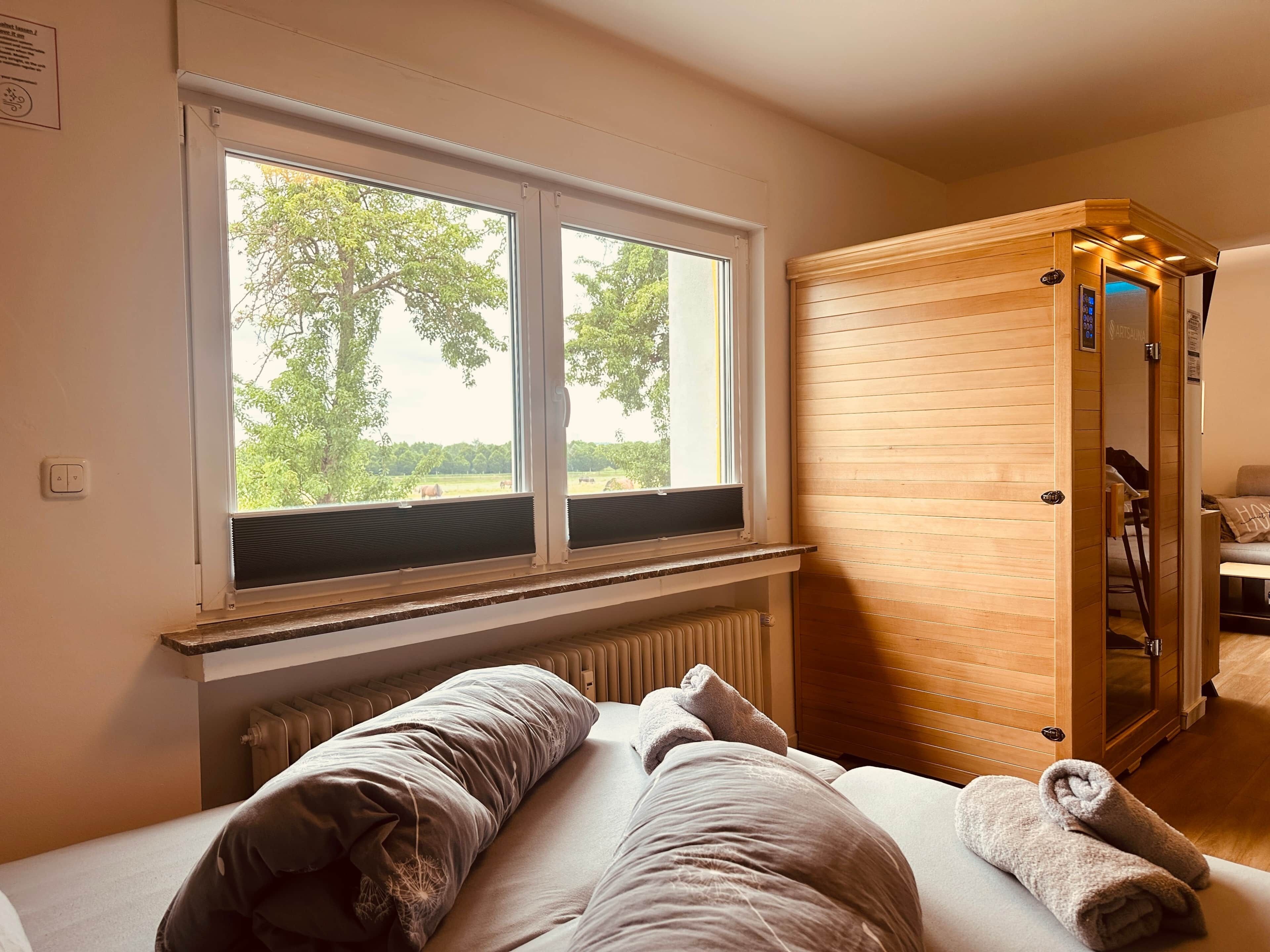 A room with a bed, a wooden sauna, and a window with a view of trees.