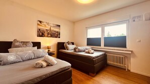 Una camera da letto con due letti, un quadro che raffigura un panorama urbano, una finestra con persiane e un termosifone.