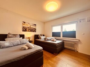 Ein Schlafzimmer mit zwei Betten, einem Stadtbild, einem Fenster mit Jalousien und einer Heizung.