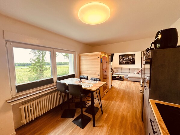 A room with a dining table, chairs, a radiator, a sofa, and a view of the outdoors.