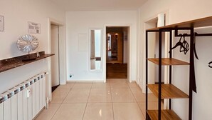 Un corridoio con parete bianca, termosifone, una mensola con oggetti decorativi e una scaffalatura in legno con elementi appesi.